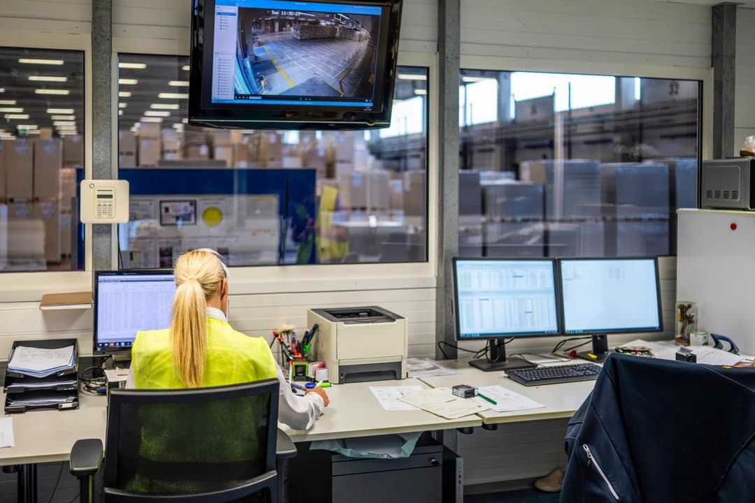 A warehouse office overlooking the floor, with monitors showing live operations